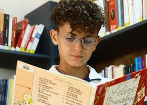 Top: Boy reading a book in a library. Bottom: Three children smiling together.