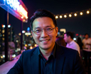 Man with john lennon glasses smiling in a cityscape at night