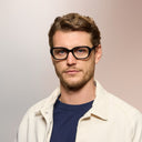 A man wearing black framed eyeglasses on a pink background. 