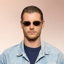 Front angle of a man wearing black sunglasses on a pink background. 