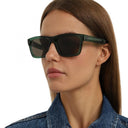 Side angle of a woman wearing dark green framed eyeglasses on a white background. 