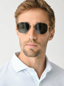 A man wearing gold framed sunglasses on a white background.