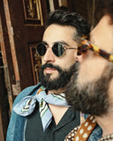 Side angle of a man wearing gold framed sunglasses with dark lenses. 